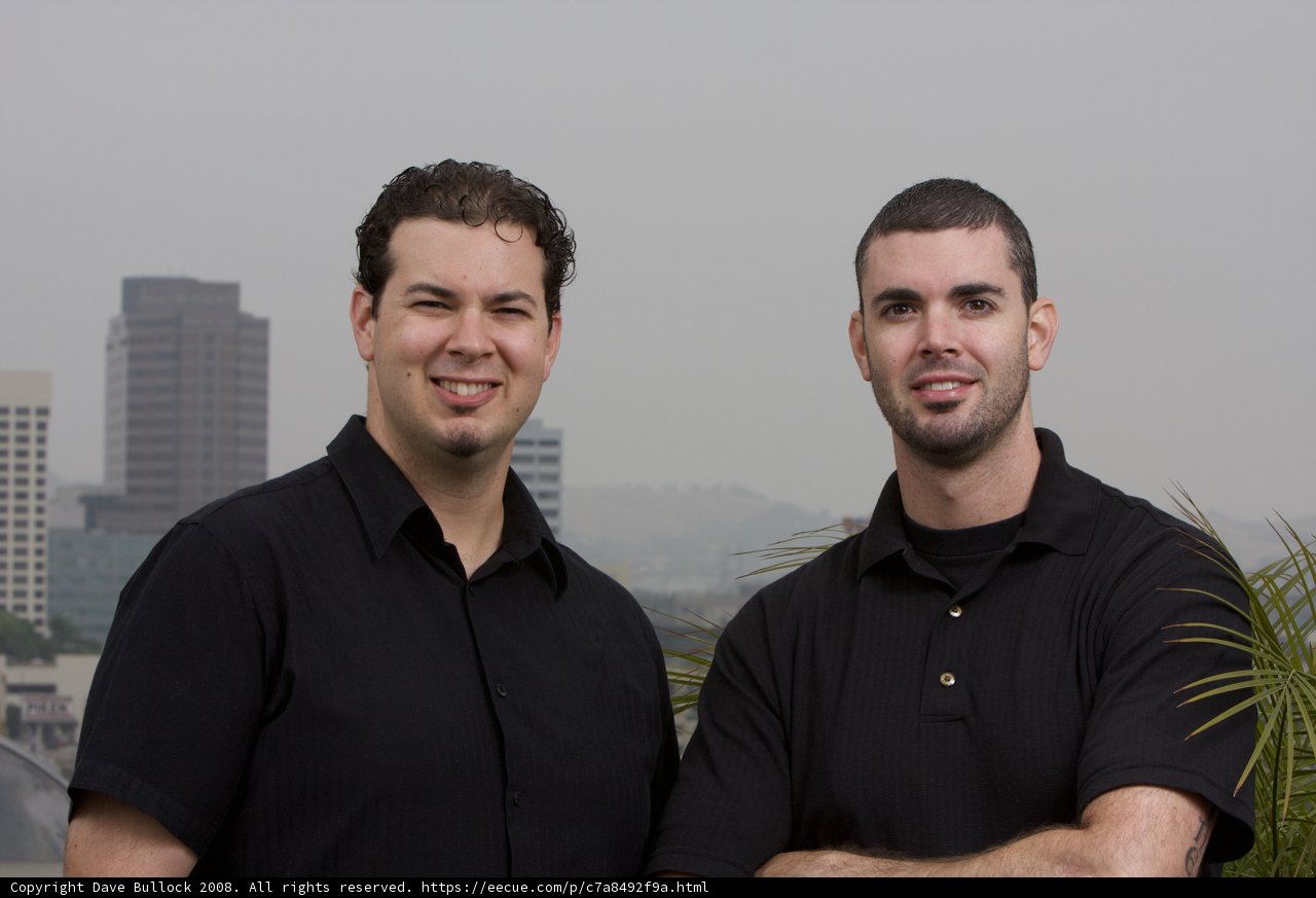 Smiling Men in Black Shirts Pose in Front of City Skyscraper