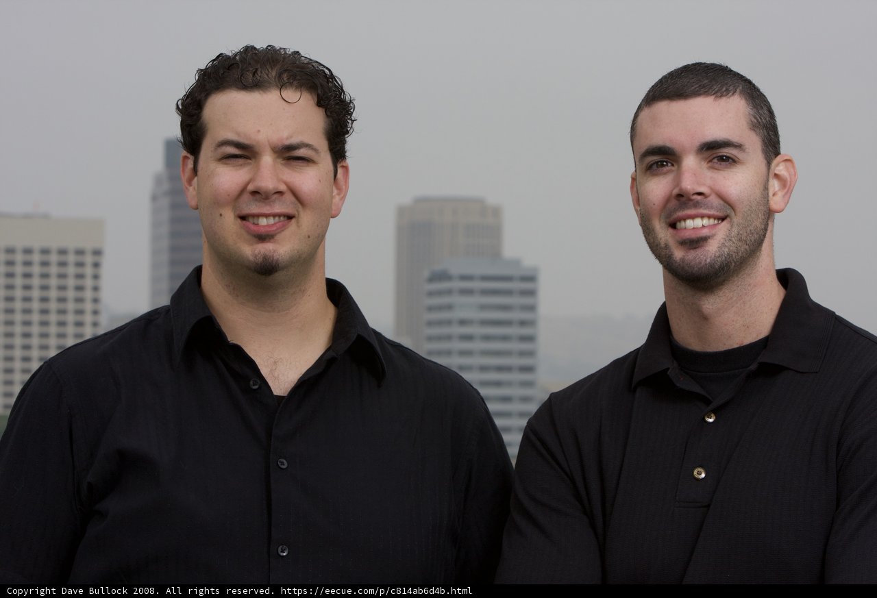 Two Happy Men in Black Shirts Pose in front of Skyscraper