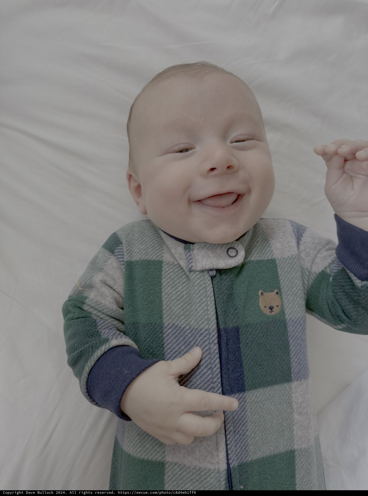 Smiling Baby in Plaid Sleeper on White Bedding