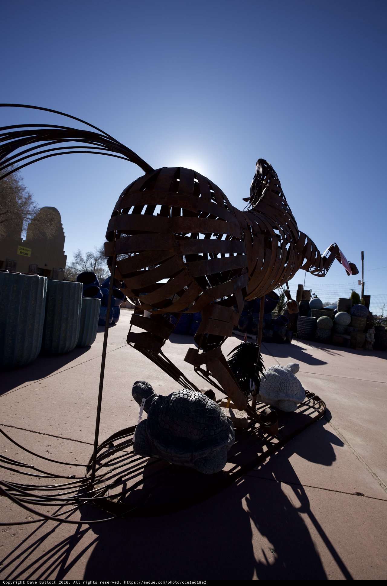 Metallic Rooster Sculpture Silhouetted Against Bright Sun