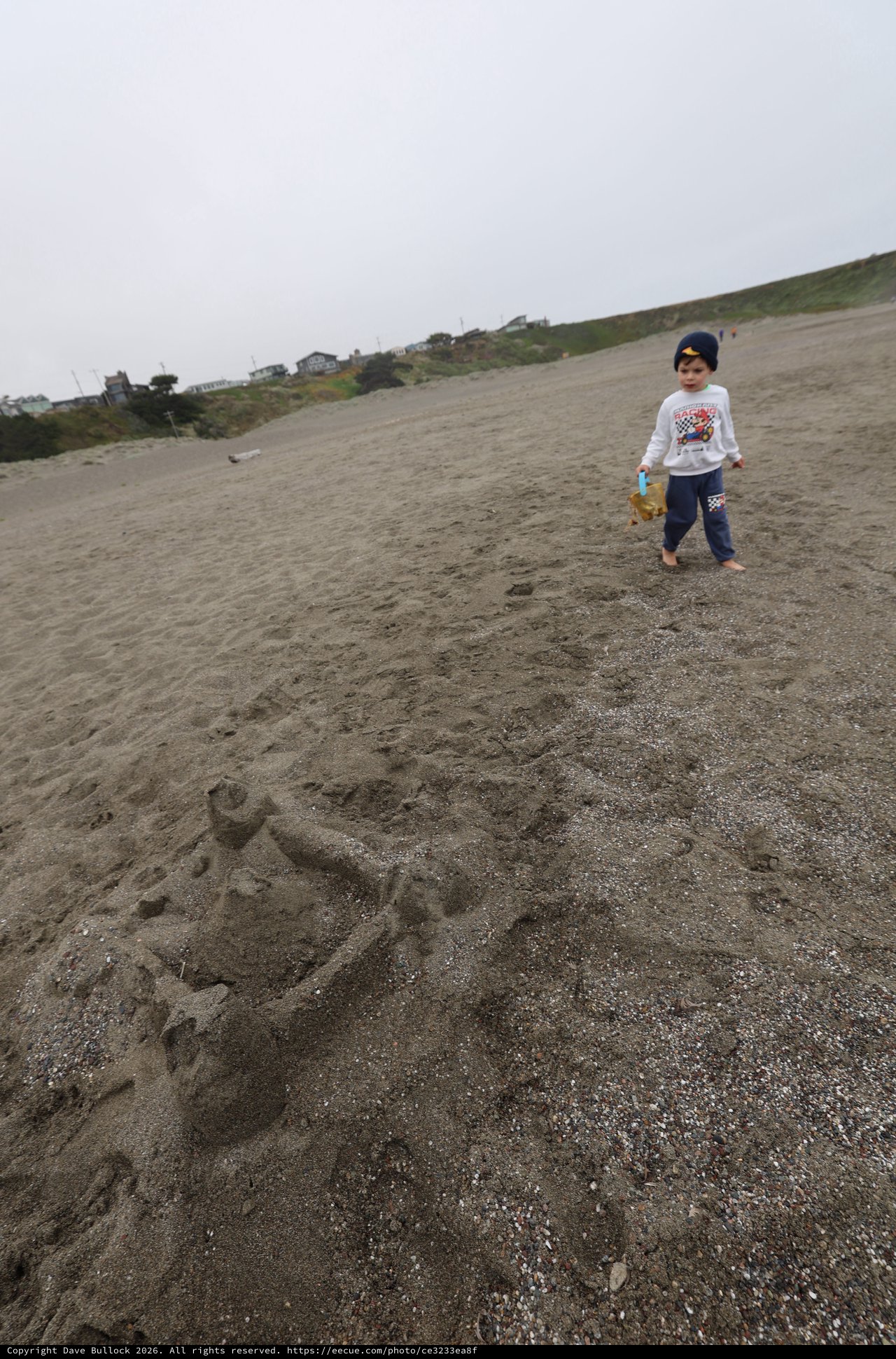 Young Boy Explores Sandy Beach with Sand Castle