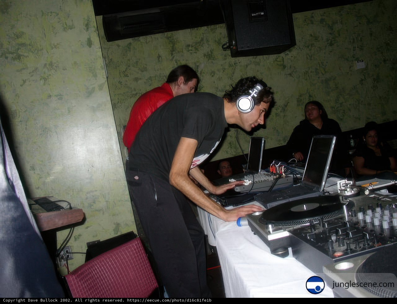 Grooving to the Beats Caption: A man in headphones enjoying the music at a party with a DJ and speakers.