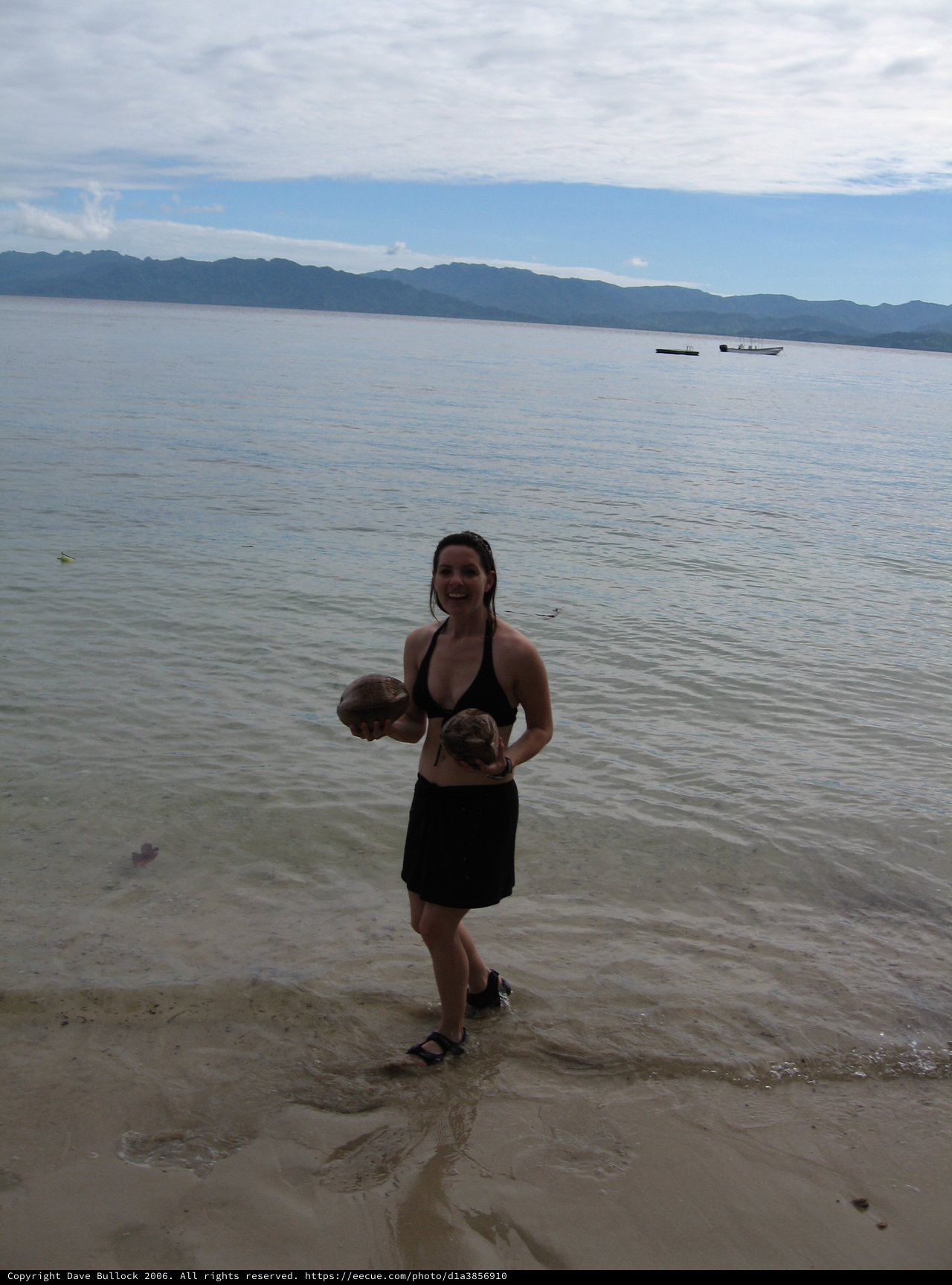 Smiling Woman Holding Coconuts on Fijian Shore