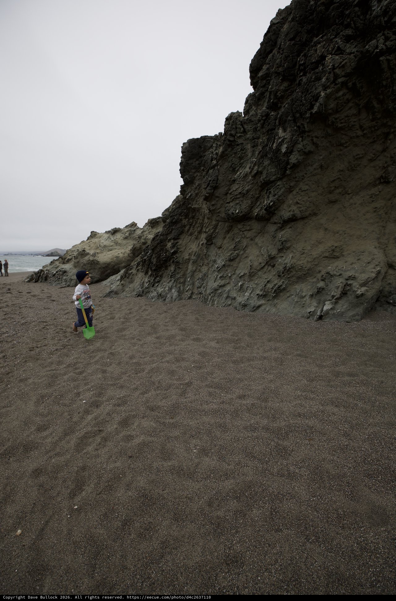 Child Explores Dark Sand Beach Beside Dramatic Cliffs