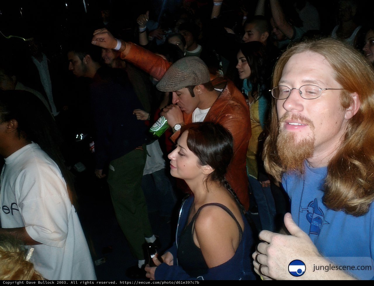 Man with Long Hair and Glasses Stands before Excited Crowd