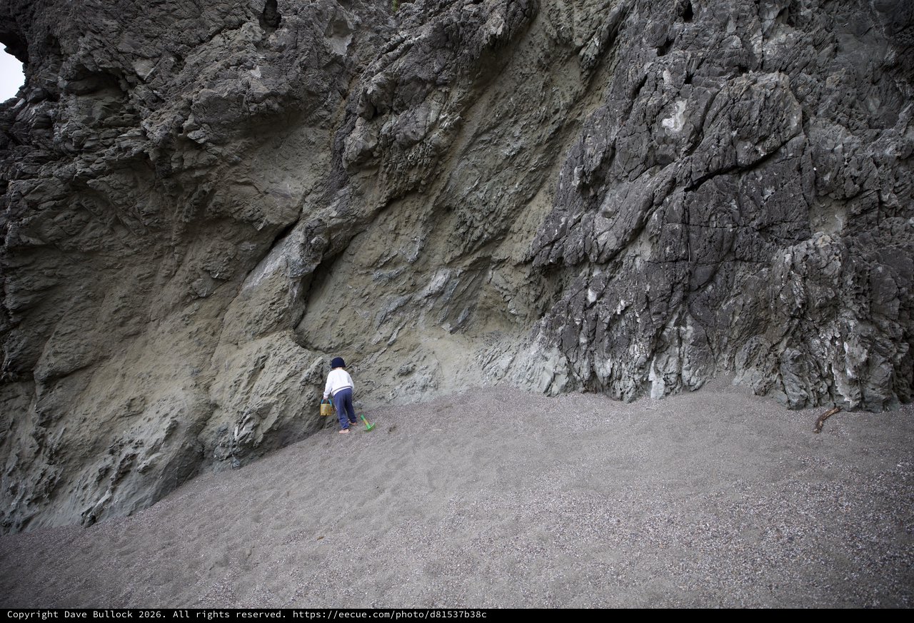 Small Child Explores Towering Sea Cliff at Low Tide