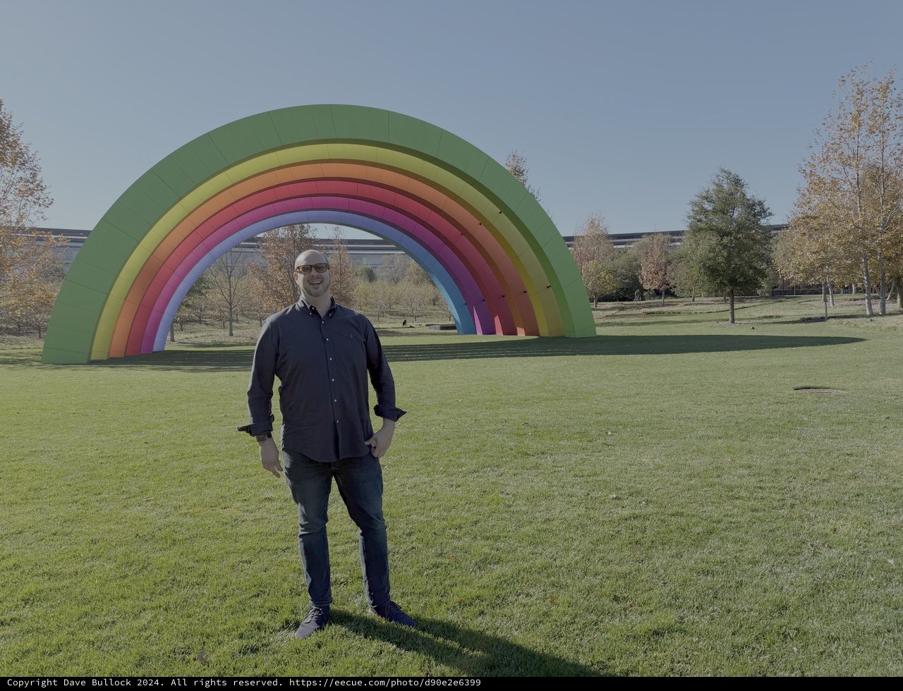 Man Poses by Large Rainbow Art Installation