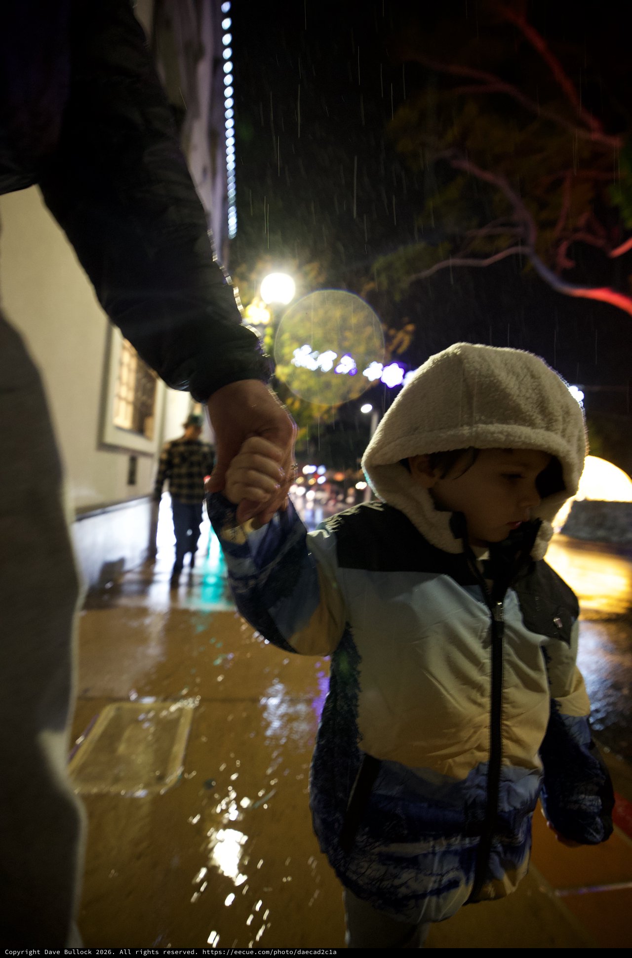 Child Walking Through Rain on Illuminated Street at Night
