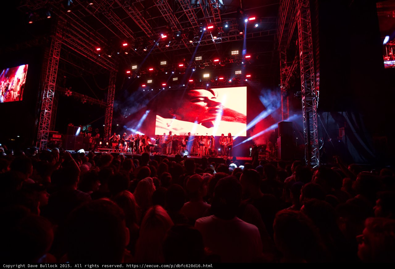 Belle and Sebastian Wide Stage Video Screen Face Profile Red Lighting Spotlight Ensemble Crowd