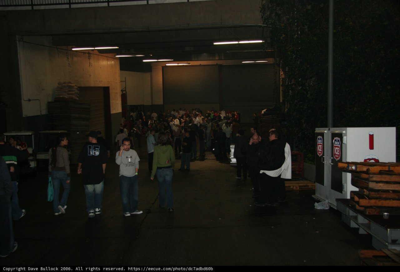 Group of People in a Parking Lot Caption: John Petrucci (center) stands among a crowd of 20 people wearing jeans and various accessories, outside a factory building in New York on New Year's Eve of 2005.