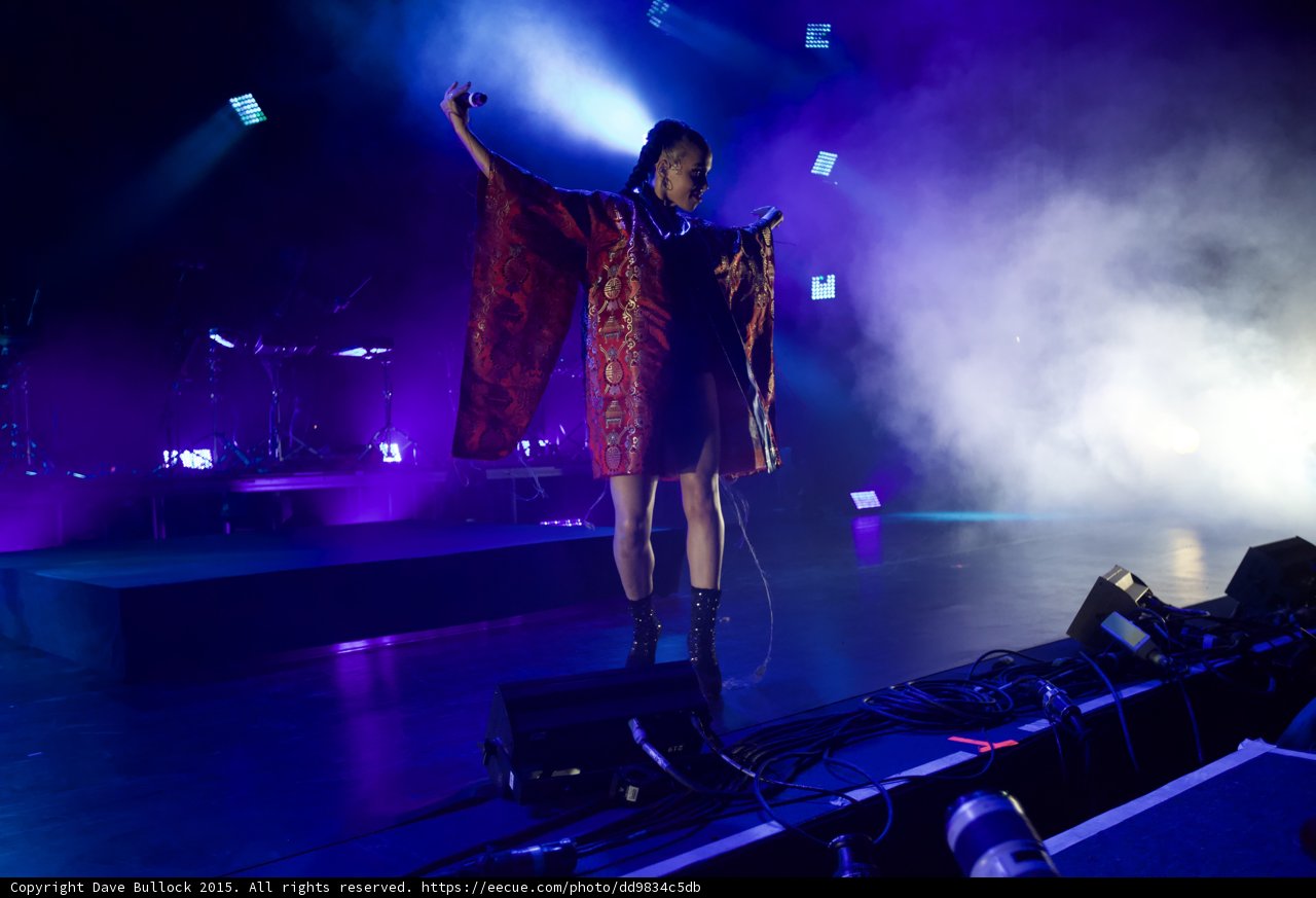 FKA twigs Full Body Arms Spread Kimono Wings One Arm Raised Microphone Red Brocade Gold Patterns Black Bodysuit Boots Blue Purple Lighting