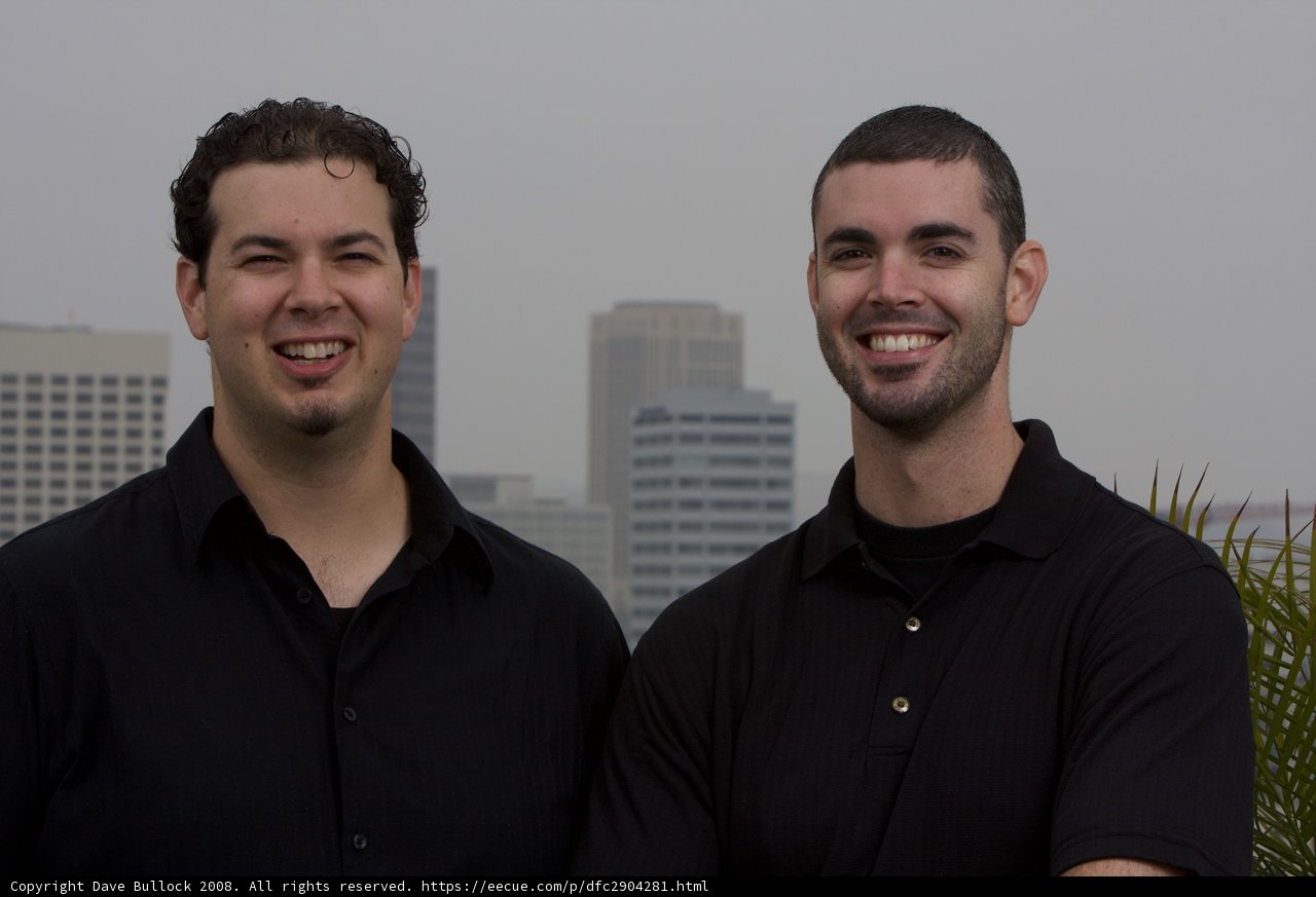 Two Happy Men in Black Shirts posing in front of a Skyscraper