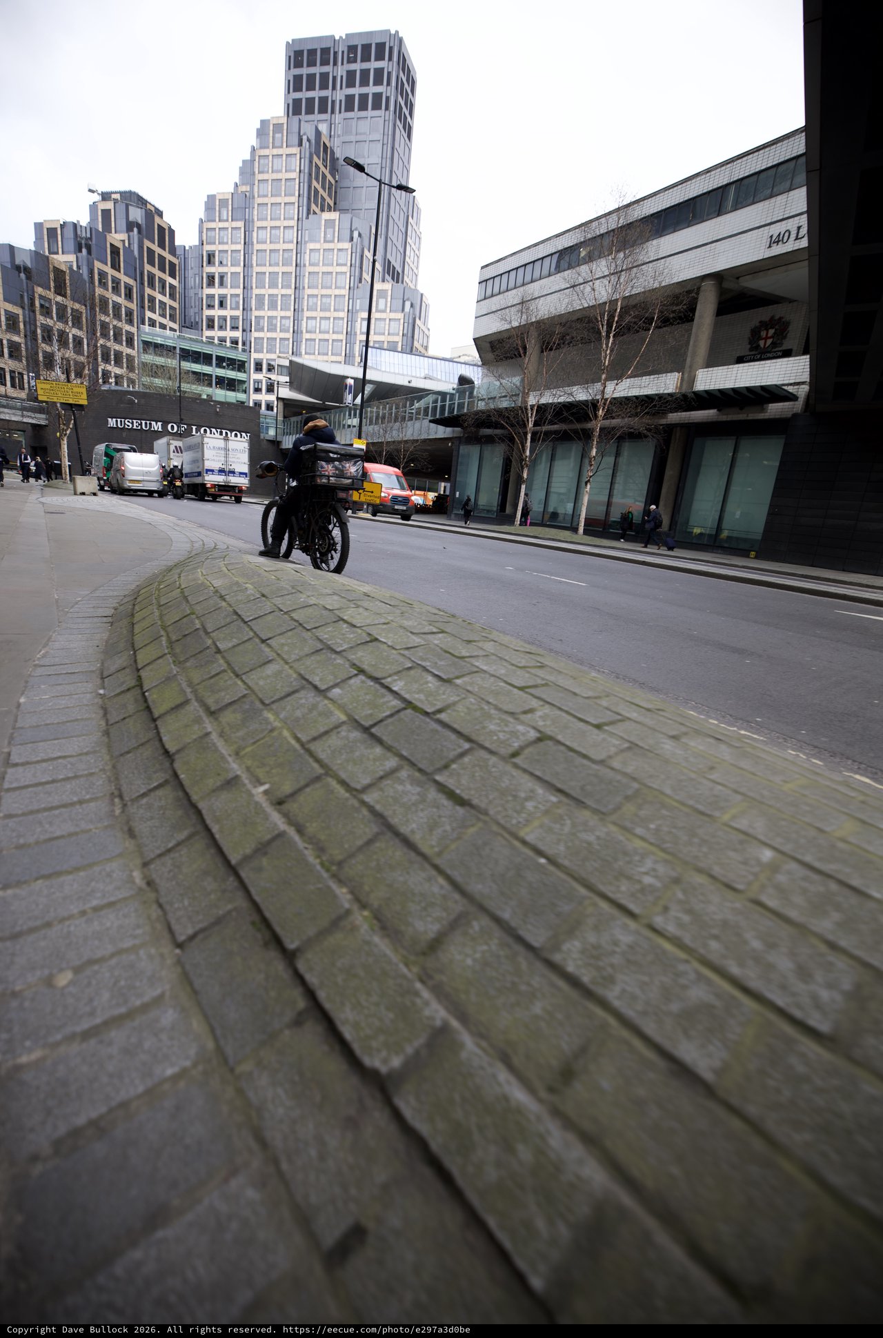 Motorcyclist Rides Past Museum of London in Urban Scene