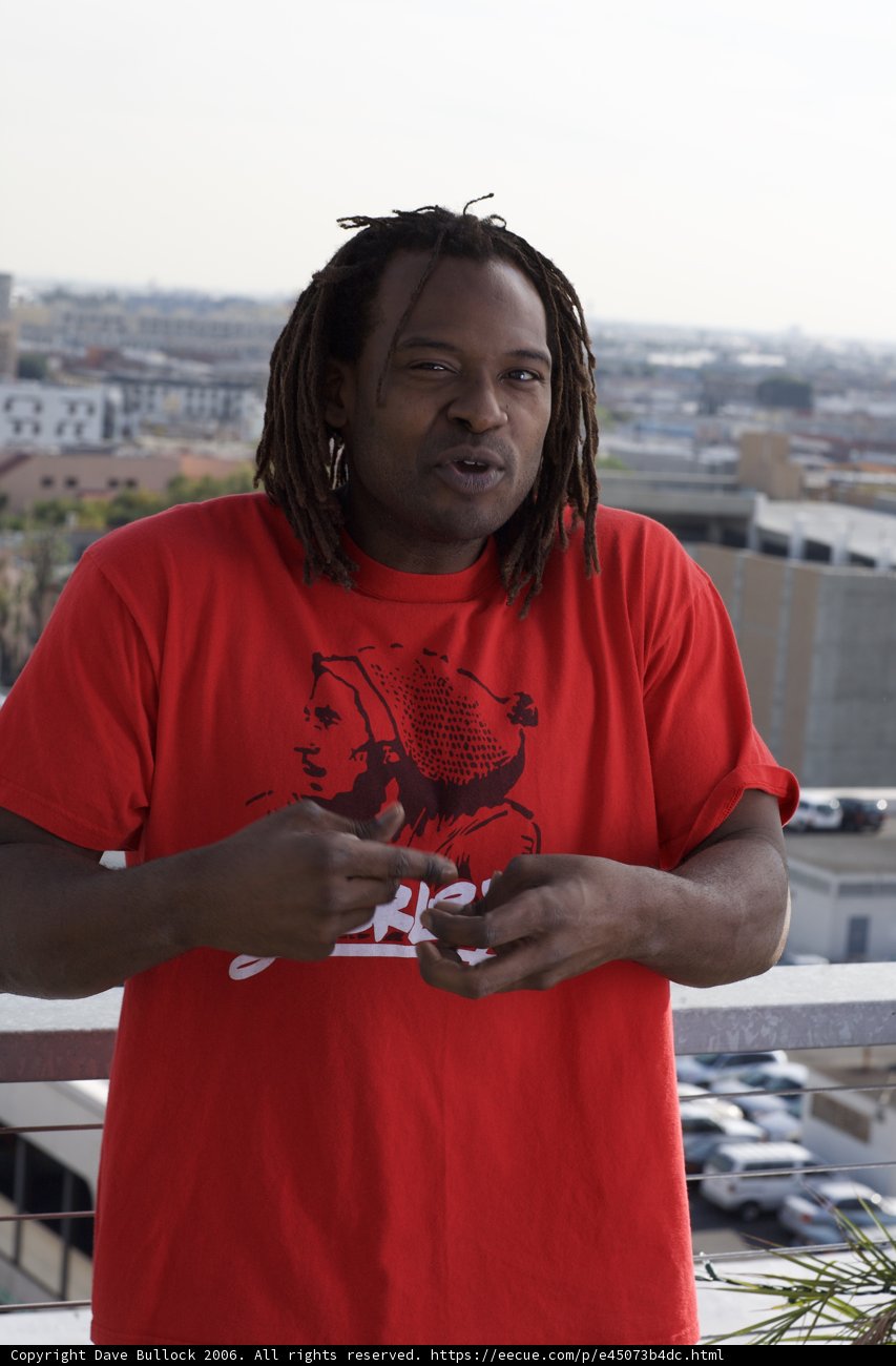 Smiling Man in Red T-Shirt Poses in Front of Buildings and Cars