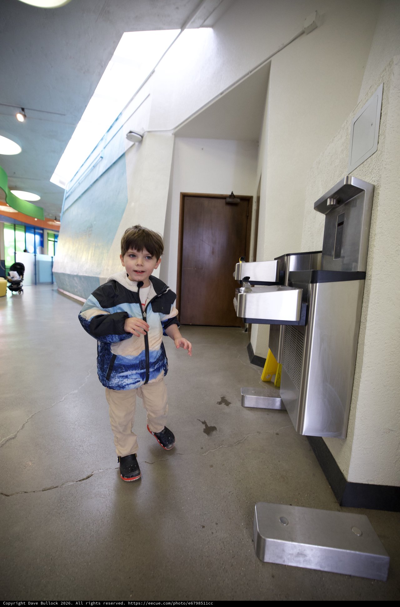 Young Boy Walking Past Water Fountain in School Hallway