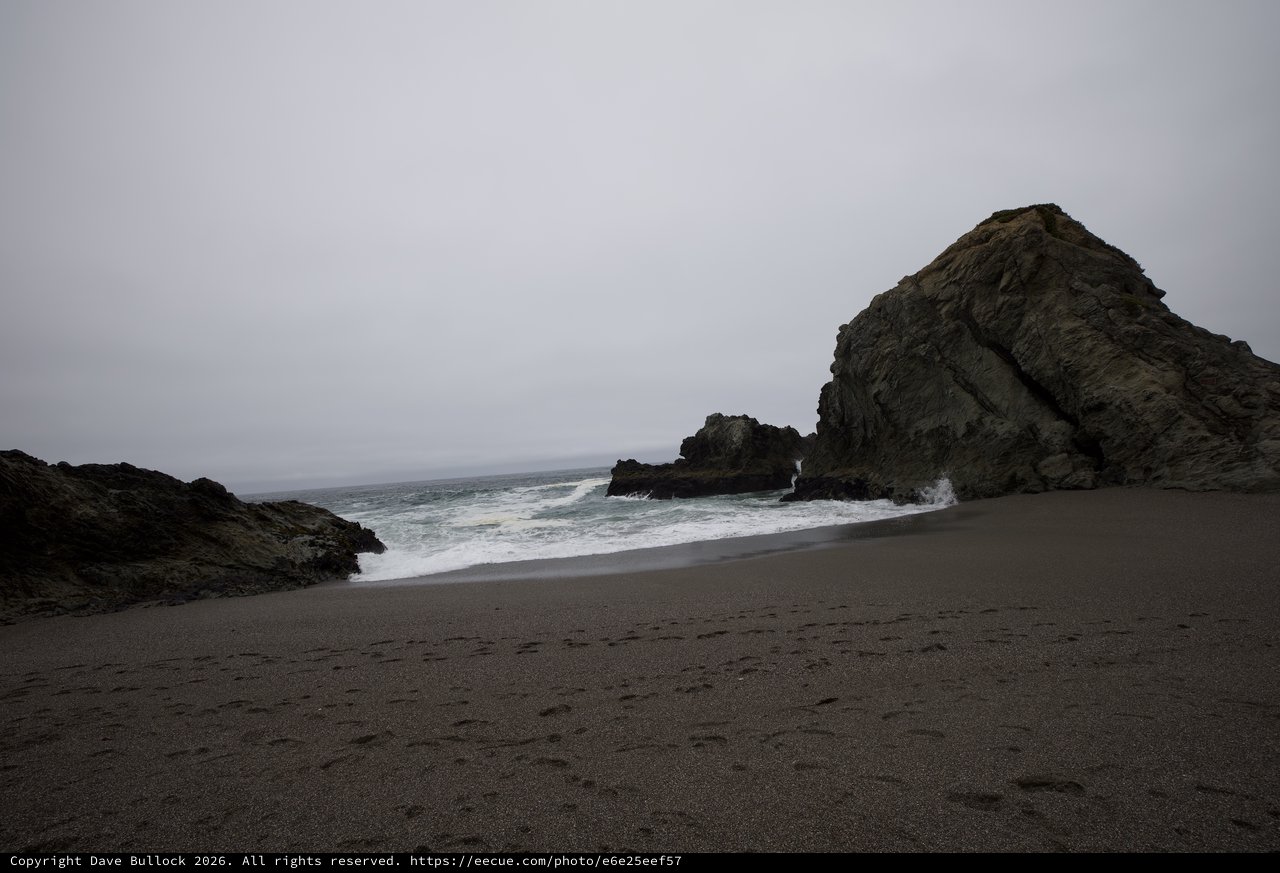 Moody Coastal Cove with Dark Sand and Sea Stacks