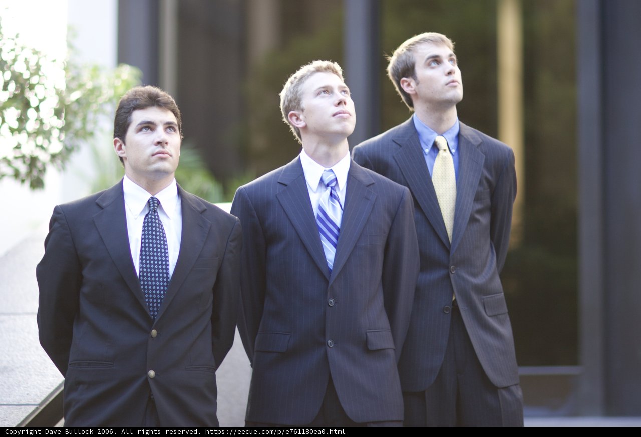 Three Men in Suits Pose in Front of Building