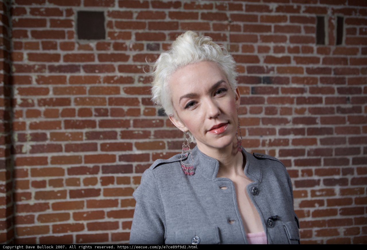 White-haired Woman in Gray Jacket Against Brick Wall