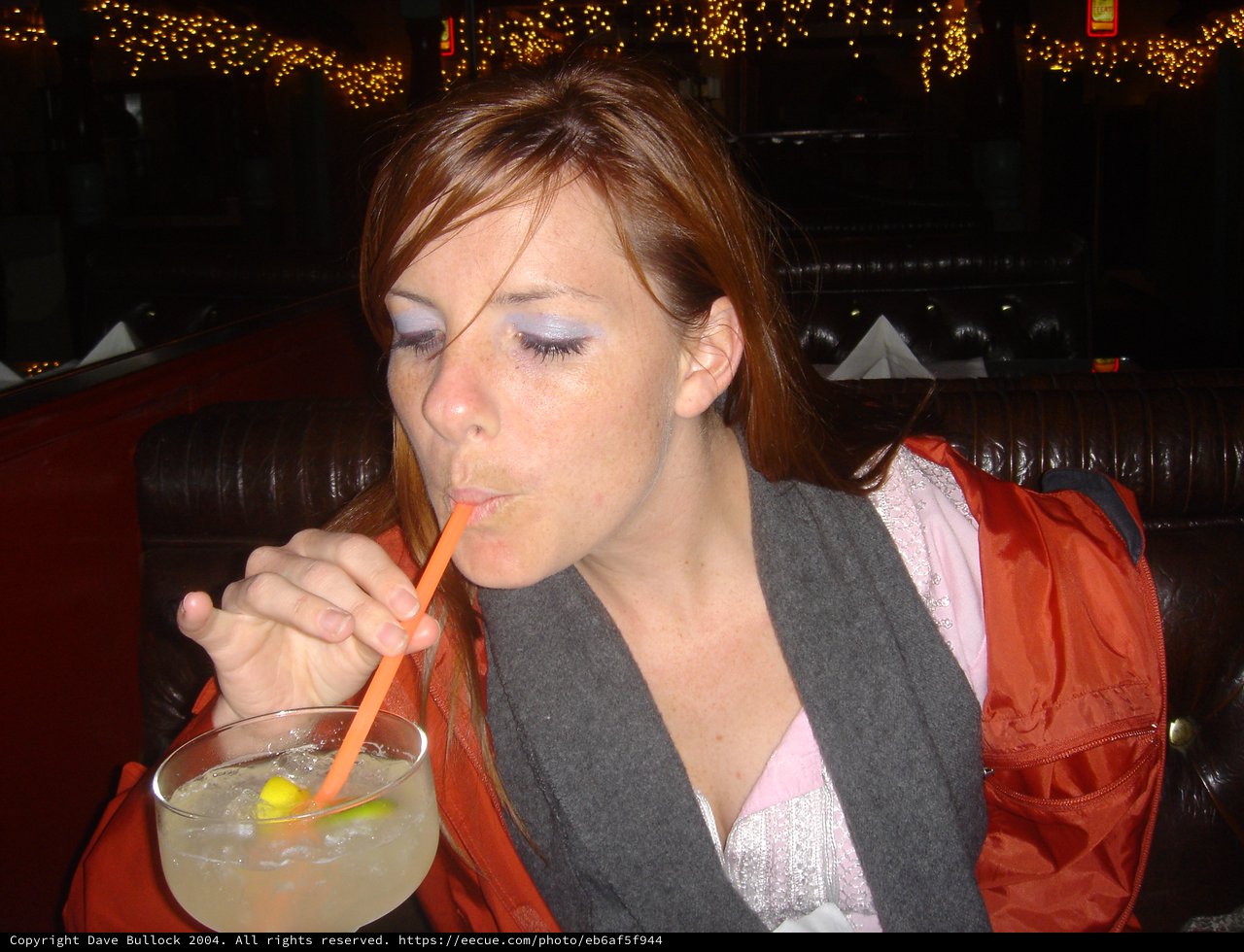 Young Woman Sipping Cocktail at Dimly Lit Bar