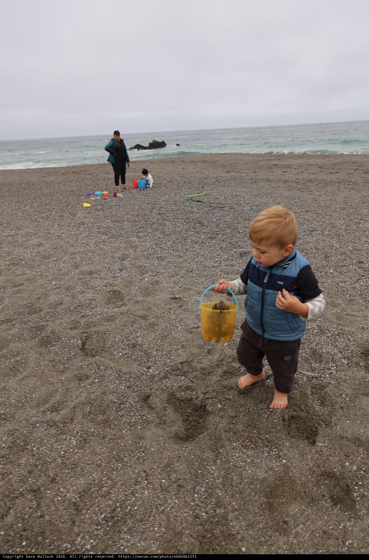 Toddler Explores Beach with Yellow Bucket