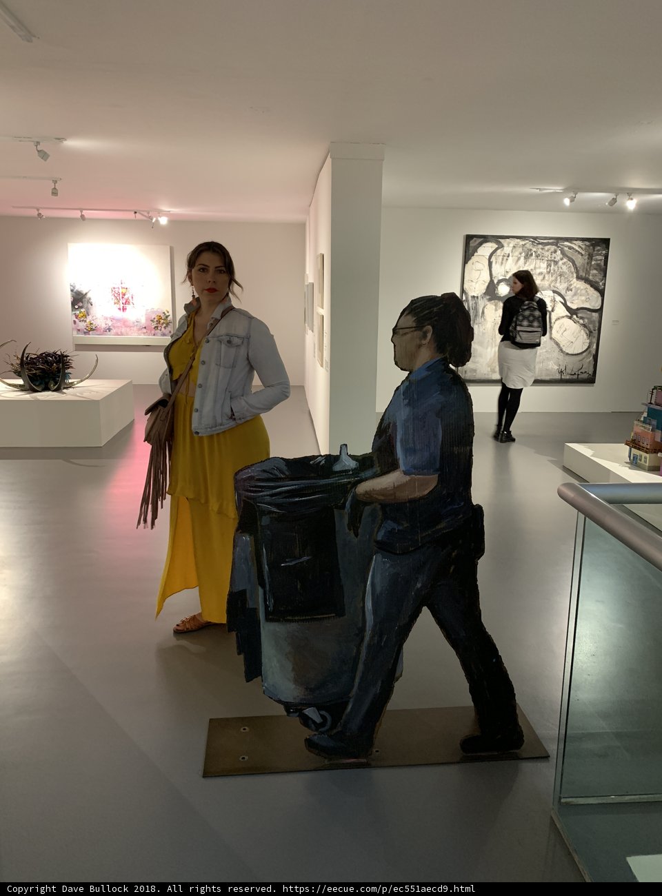 Woman carrying a trash can through an art gallery