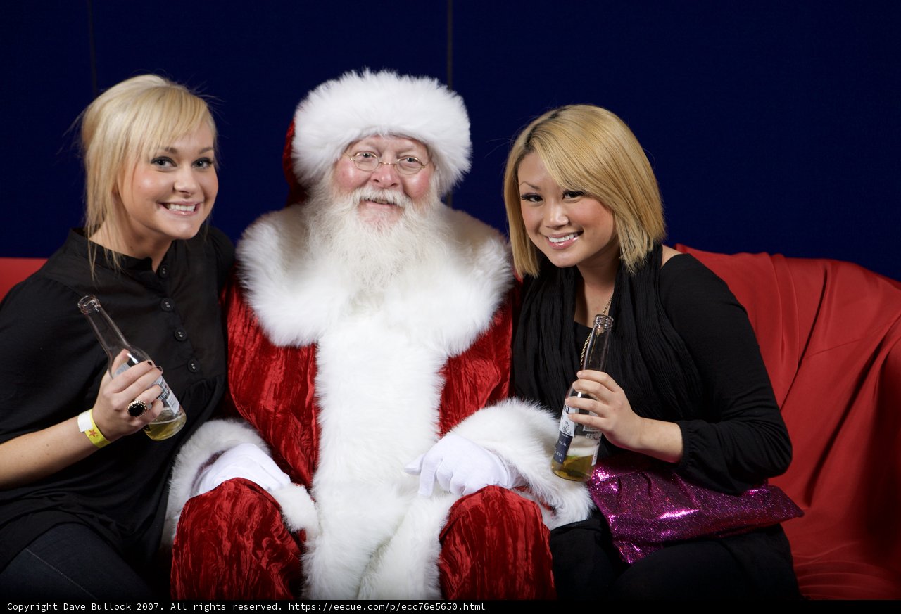 Festive Christmas Gathering Caption: Two women and a man sit on a couch, donning festive clothing and Santa Claus hats, holding glasses and a container of treats, at the 2007 APC Christmas party.