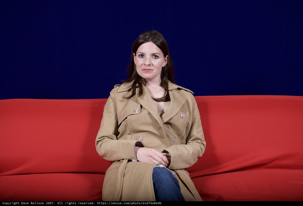 Woman in Trench Coat Seated on Red Sofa
