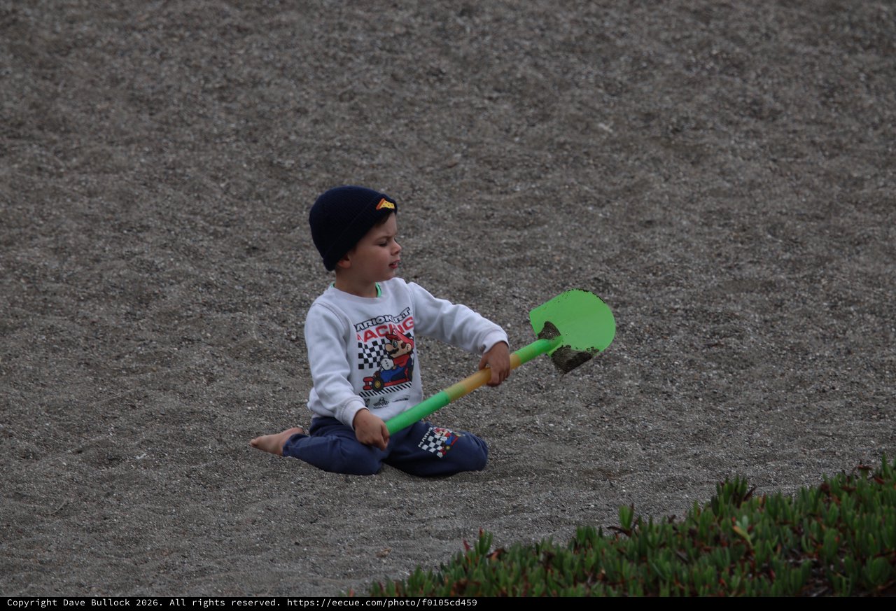 Young Boy Playing with Shovel on Sandy Beach