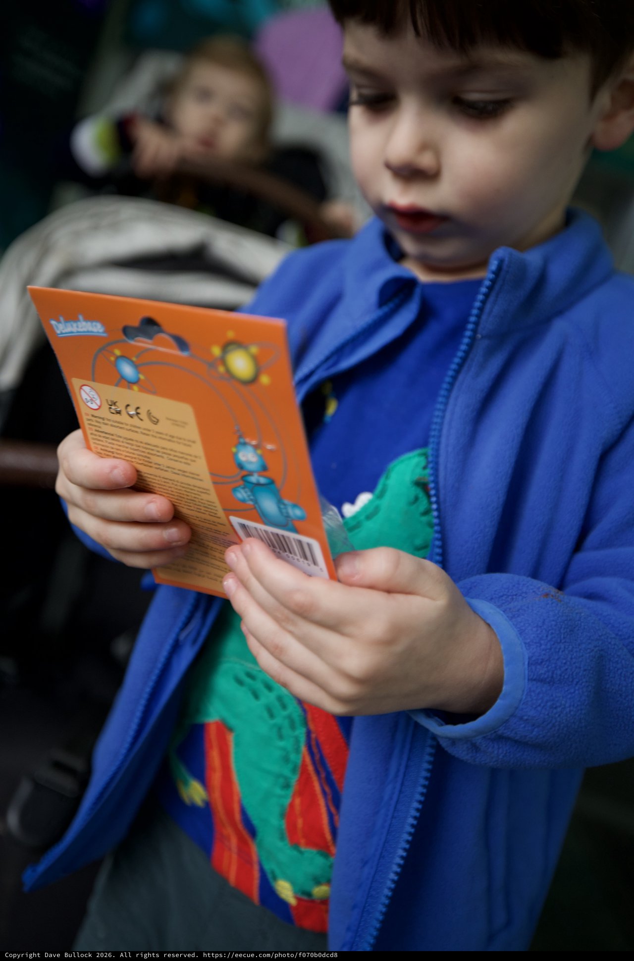 Young Boy Reading Orange Toy Package Intently