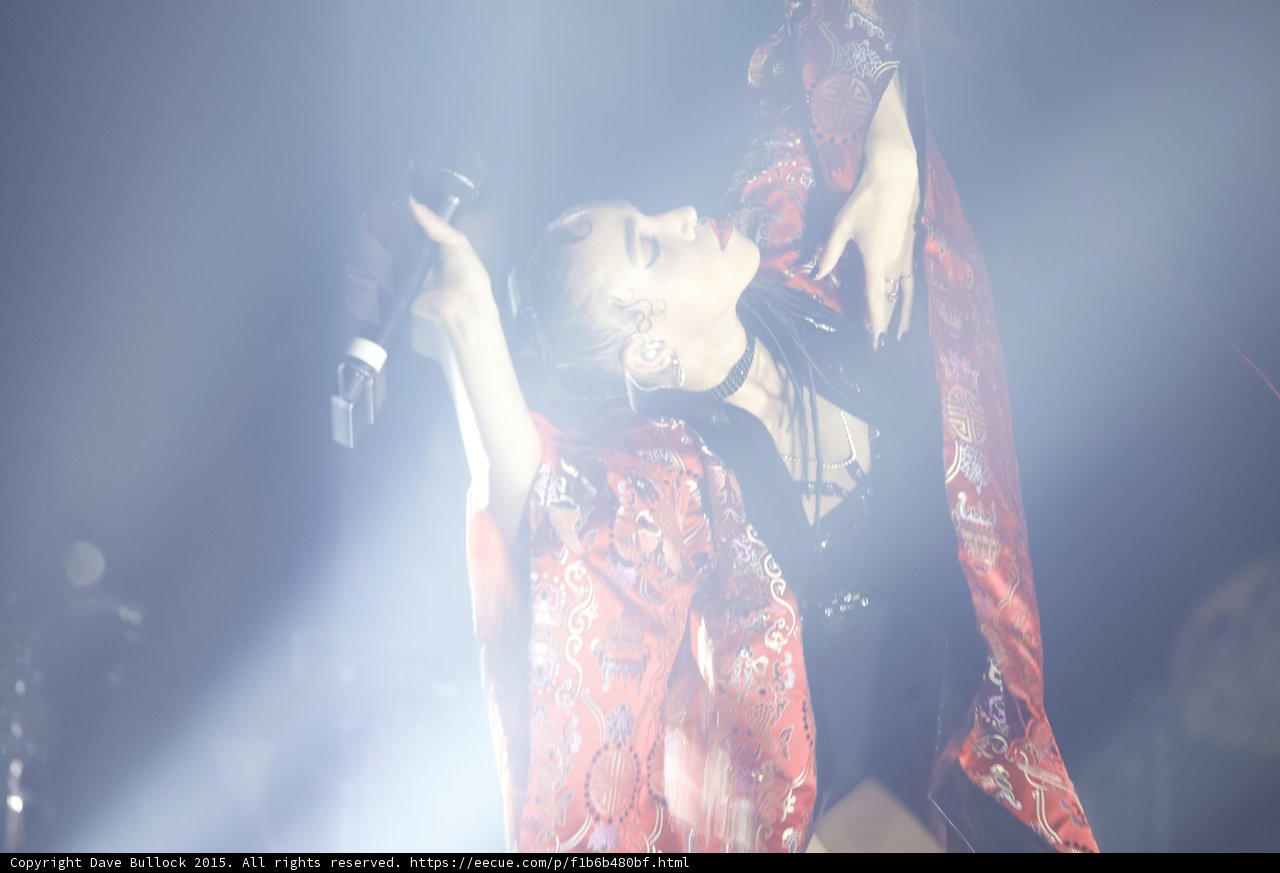 FKA twigs Looking Upward Both Arms Extended Microphone Red Brocade Kimono Black Choker Face Illuminated