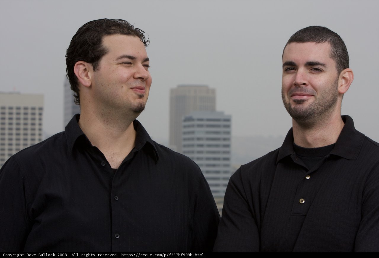 Two Happy Men in Black Shirts Pose in Front of Skyscraper