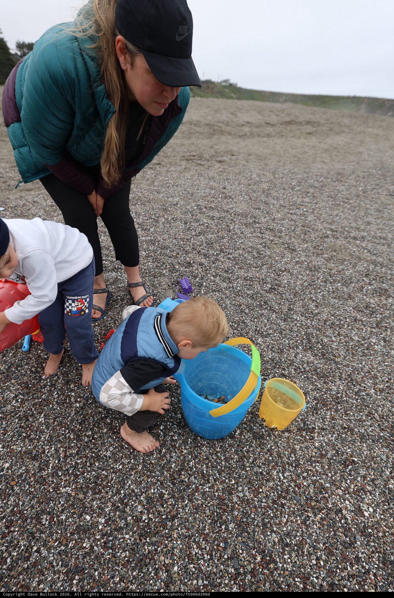 Toddler Explores Beach Bucket on Rocky Shore