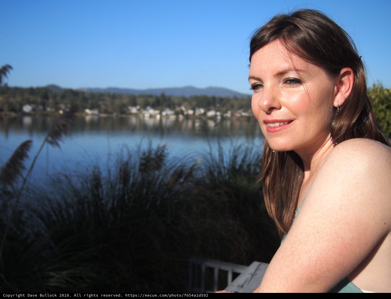 Woman Smiling by a Tranquil Lakeside on Sunny Day