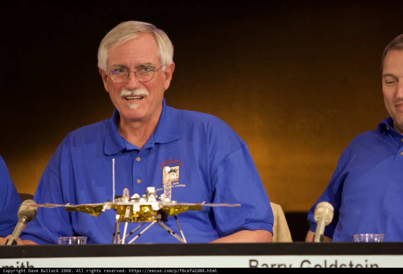Blue-Shirted Trio Examines Mysterious Gold Object at Phoenix Landing Press Conference