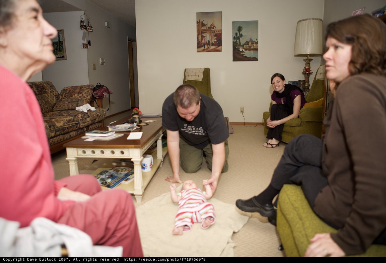 Family Gathers Around Newborn Baby on Living Room Floor