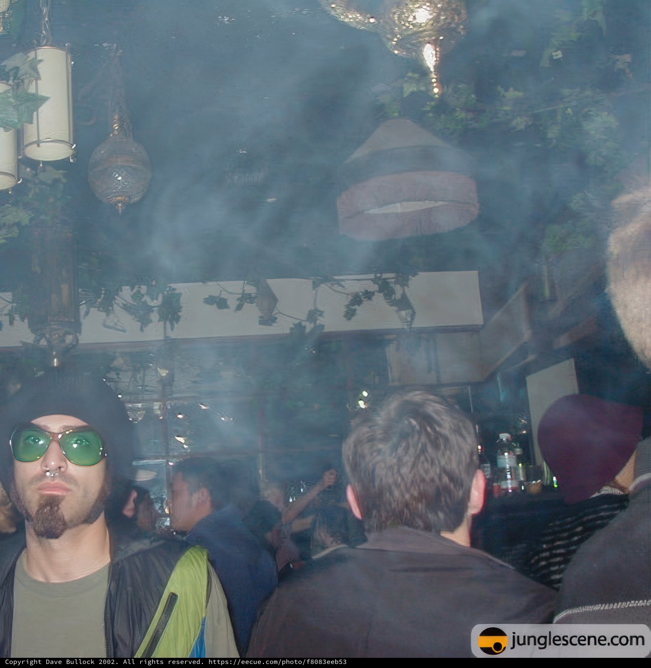 Man in Sunglasses and Hat Stands Among Nightclub Crowd