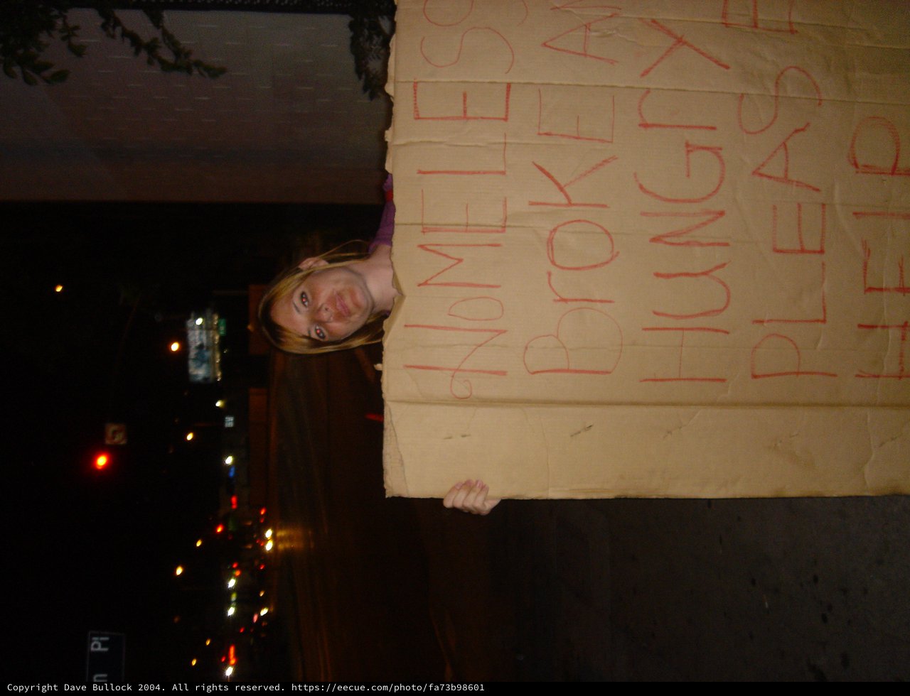 Woman Holds Humorous Homeless Cardboard Sign at Night