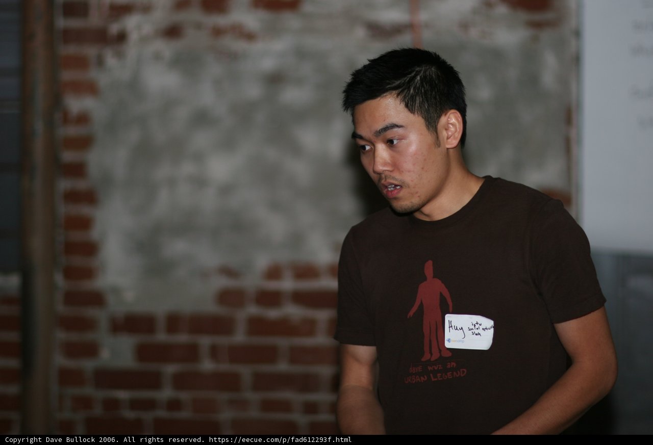Brown Shirted Man Stands Tall in Front of Brick Wall