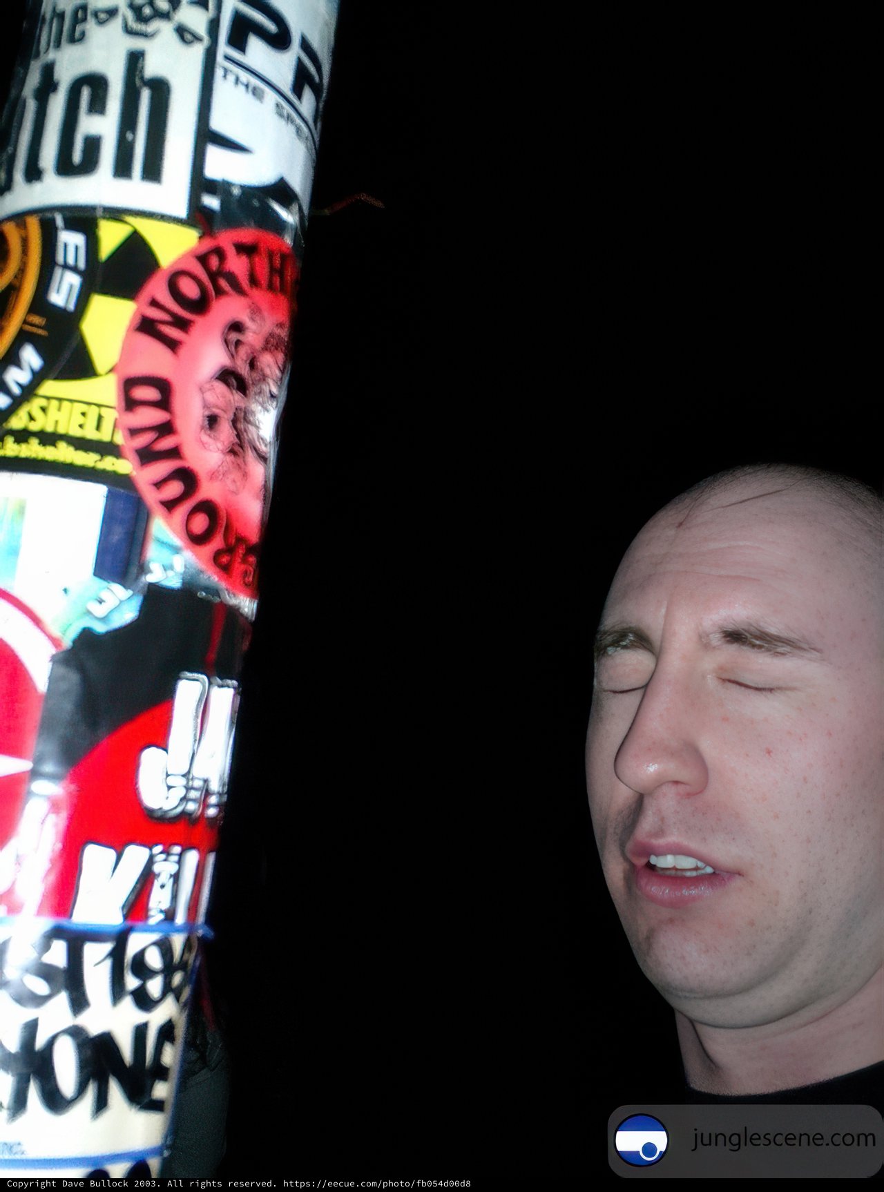 Black Shirted Eric Poses with Sticker Sign