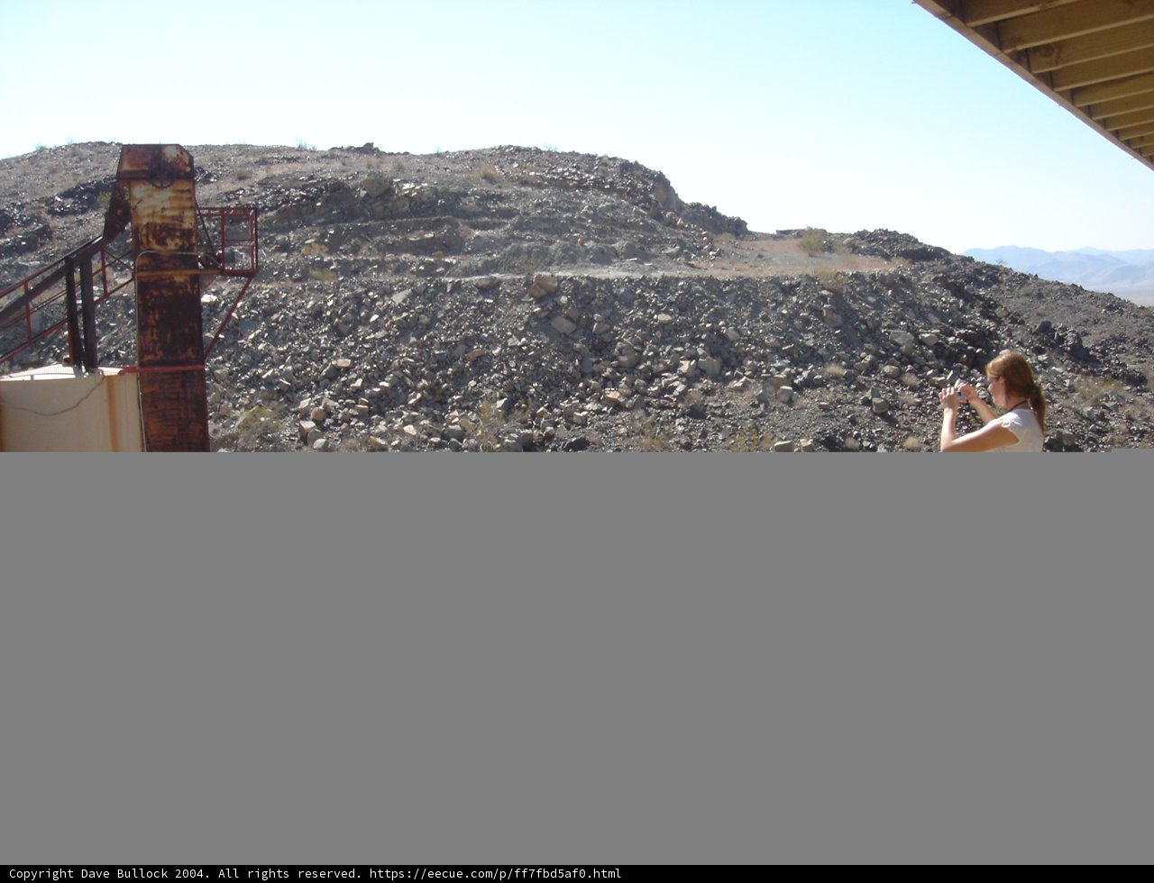 Summit Views Caption: A woman takes in stunning mountain vistas, standing atop a rocky outcropping and holding onto the handrail for balance. The bright blue sky and rugged landscape make for a picturesque wilderness scene.