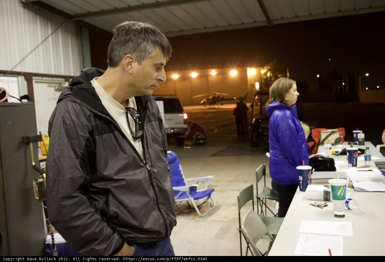 Man dressed in coat standing next to wooden table with cup of coffee