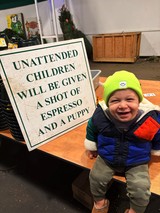 Joyful Toddler at Coffee Shop with Humorous Warning Sign