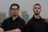 Two Happy Men in Black Shirts Pose Outside Skyscraper