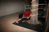 Sitting on the Sidewalk Caption: A man sits on the sidewalk, his hand resting on the tree trunk beside him.