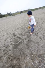 Young Boy Explores Gray Sand Beach with Bucket