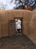 A Woman Stands Before An Adobe Door