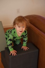Toddler in Green Dinosaur Pajamas Playing on Ottoman