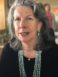 Gray-haired woman wearing a bead necklace and glasses