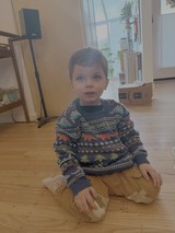 Young Child in Dinosaur Sweater Sitting on Floor