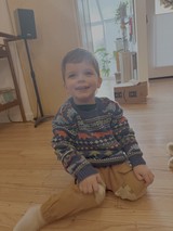 Happy Toddler in Dinosaur Sweater Sitting Indoors